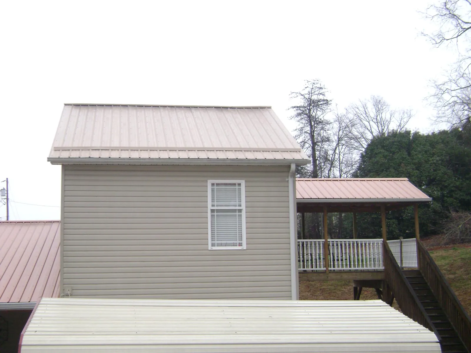 Tan metal roofs on a two story addition and attached porch, from a Roof Replacement job in Evans